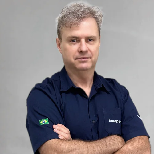 Adalton vendedor caminhao de braços cruzado, sorriso e sua camisa é da cor azul marinho.