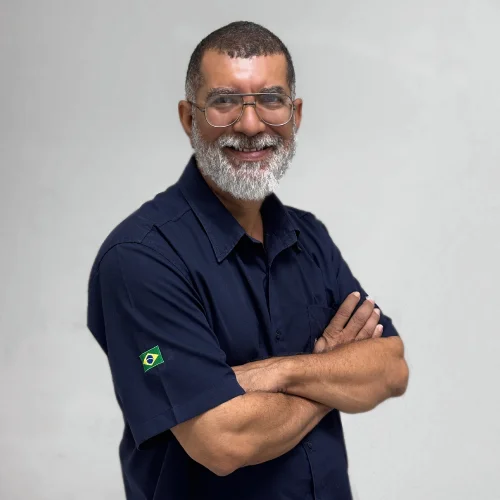Ademir vendedor caminhao de braços cruzado, sorriso e sua camisa é da cor azul marinho.