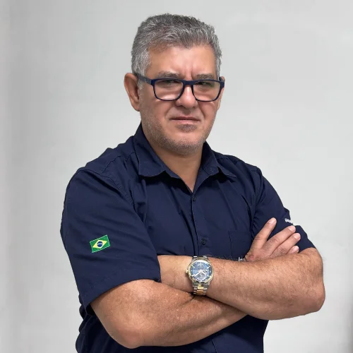 Ivo vendedor caminhao de braços cruzado, sorriso e sua camisa é da cor azul marinho.