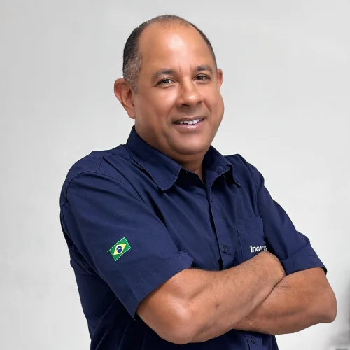 Marcelo vendedor caminhao de braços cruzado, sorriso e sua camisa é da cor azul marinho.